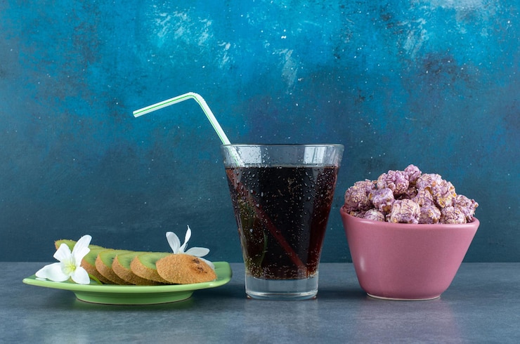 Bezpłatny plik Zdjęcie zestaw przekąsek z pokrojonych kiwi, szklanki coli i miski cukierków popcorn na niebiesko