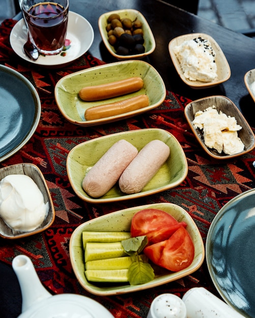 Bezpłatne zdjęcie zestaw śniadaniowy z kiełbasami, pomidorem i serem ogórkowym, czarną herbatą oliwkową