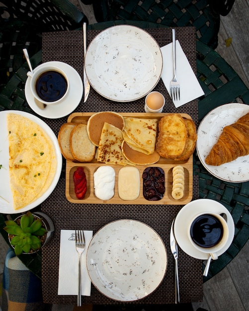 Zestaw śniadaniowy z naleśnikami, grzankami, rogalikiem, jajkiem, krojonymi truskawkami, bananami i kawą