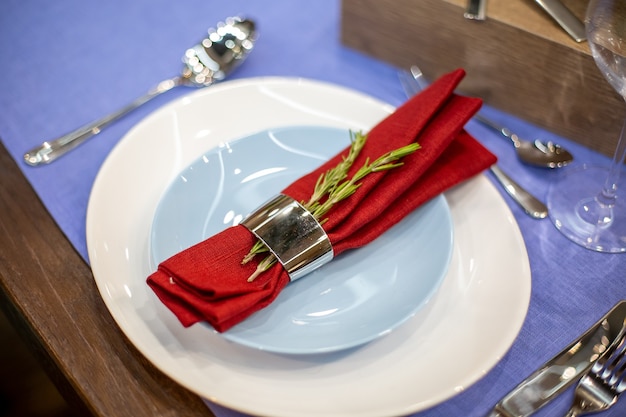 Zestaw stołowy z niebieską serwetką obrusową w stalowym uchwycie z gałązką rozmarynu