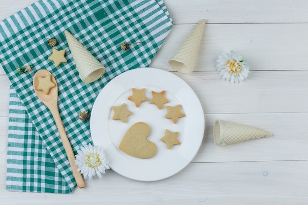 Zestaw szyszki waflowe, kwiaty i ciasteczka w talerz i drewnianą łyżką na tle ręcznik drewniany i kuchenny. leżał płasko.