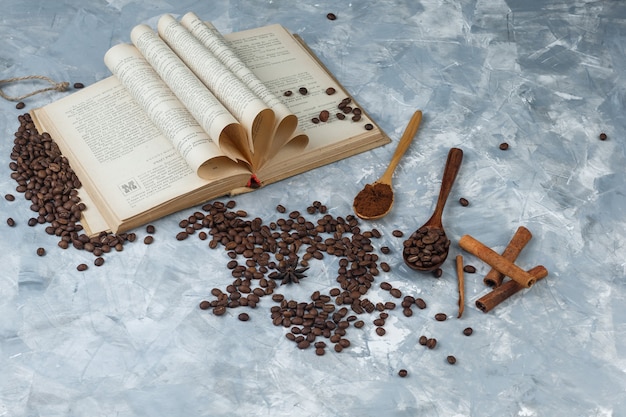 Zestaw zmielonej kawy, książki, laski cynamonu i ziaren kawy w drewnianą łyżką na nieczysty szarym tle. widok pod dużym kątem.