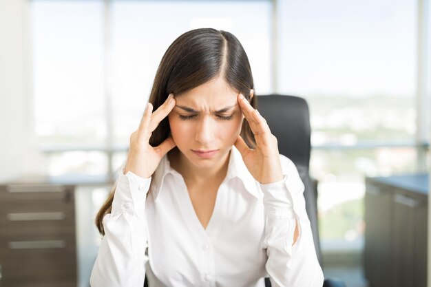Zestresowana młoda menedżerka z bólem głowy dotykającym skroni w biurze