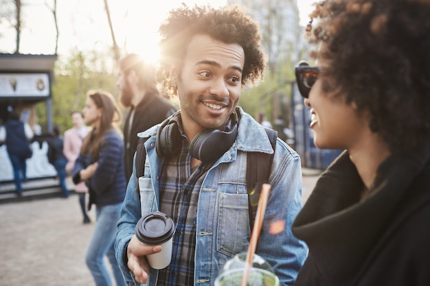 Zewnątrz portret afroamerykańskich przyjaciół spaceru w parku podczas rozmowy i picia kawy, na sobie modne ubrania.