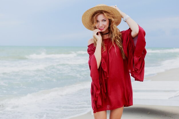 Zewnątrz portret całkiem biały imbir kobieta w stylowej sukience pozowanie na plaży w pobliżu oceanu. Błękitne niebo. Wietrzna pogoda.