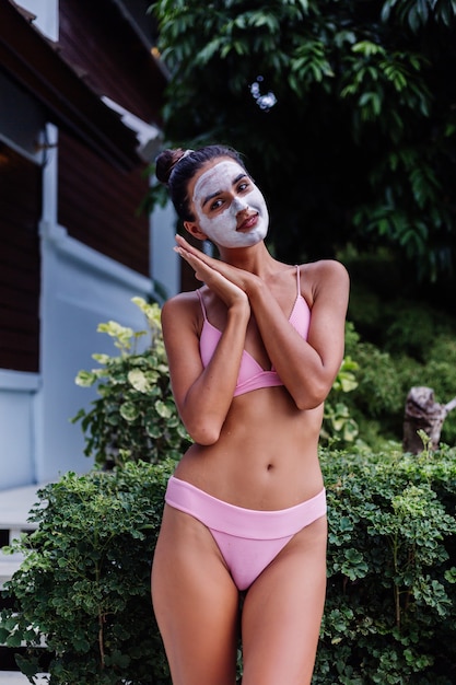 Zewnątrz portret opalonej skóry spokojny dość kaukaski kobieta w bikini w spa z białą maską peeling na twarzy