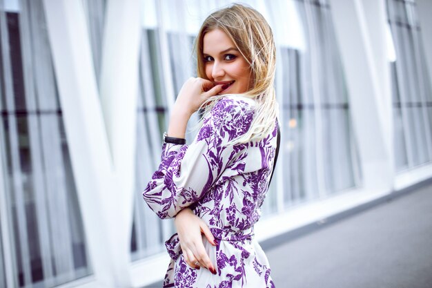 Zewnątrz portret podekscytowanej uśmiechniętej blondynki na sobie elegancką modną sukienkę w kwiaty i patrząc w kamerę, wiosna lato.
