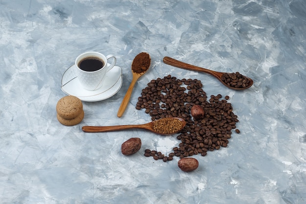 Ziarna kawy, filiżanka kawy z kawą rozpuszczalną, mąka kawowa, ziarna kawy w drewnianych łyżeczkach, ciasteczka pod wysokim kątem na jasnoniebieskim marmurowym tle