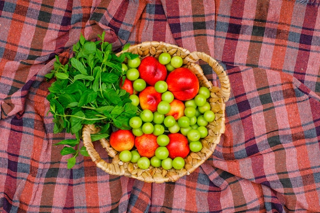 Zieleni i brzoskwinie z liśćmi w wiklinowym koszu na tkaniny piknikowej. widok z góry.