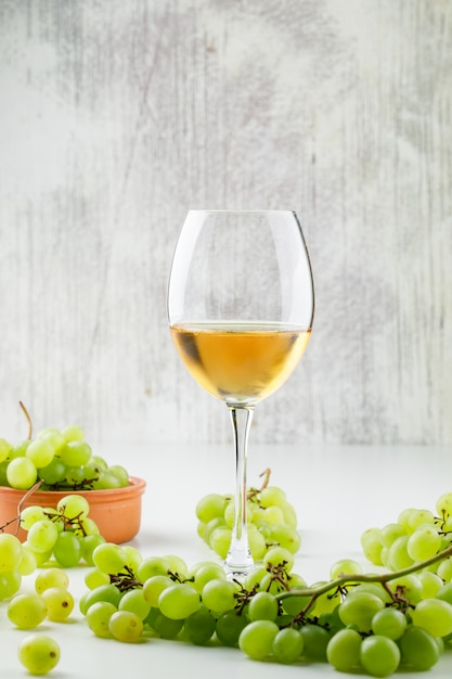 Bezpłatne zdjęcie zieleni winogrona z winem w czara w glinianym talerzu na biel powierzchni