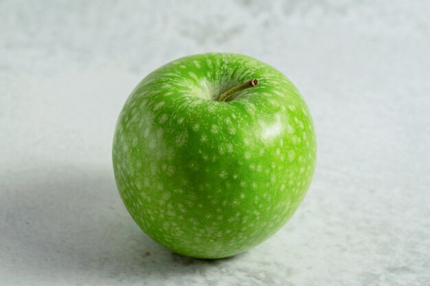 Zielone, ekologiczne, świeże jabłko. Na szarej powierzchni.