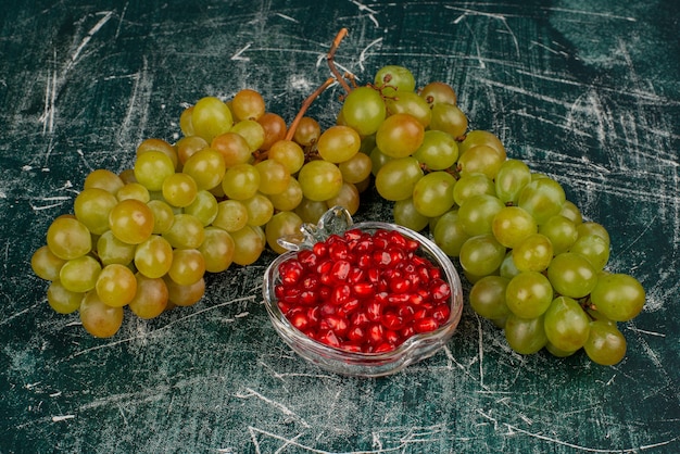 Bezpłatne zdjęcie zielone winogrona i pestki granatu na marmurowej powierzchni.