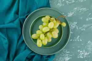 Bezpłatne zdjęcie zielone winogrona z talerzem w spodeczku na gipsie i tkaninie,