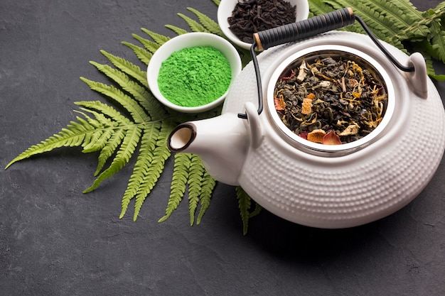 Bezpłatne zdjęcie zielony matcha herbaty proszek i suchy ziele z ceramicznym czajnikiem na czarnej powierzchni