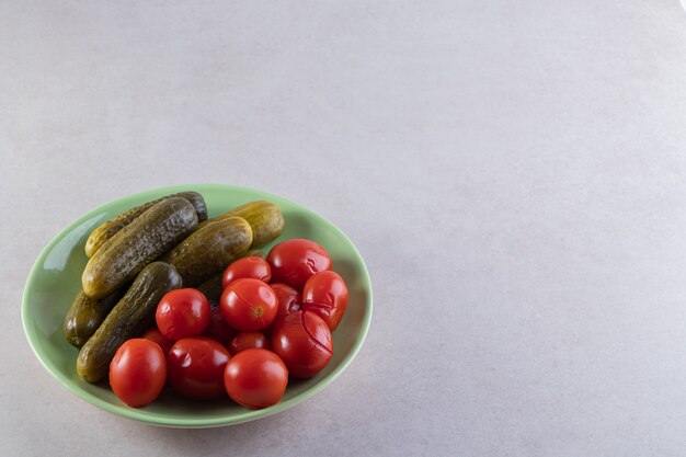Zielony talerz kiszonych ogórków i pomidorów na kamiennym stole.