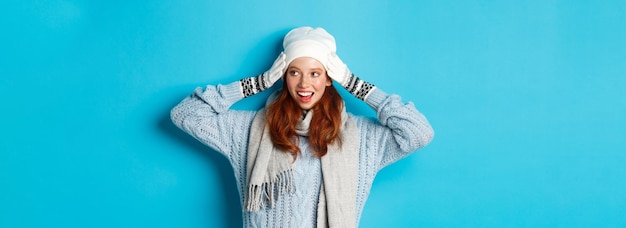 Bezpłatne zdjęcie zima i święta koncepcja szczęśliwa rudowłosa dziewczyna w czapce kapeluszu szaliku i rękawiczkach patrząc w prawo i uśmiechając się