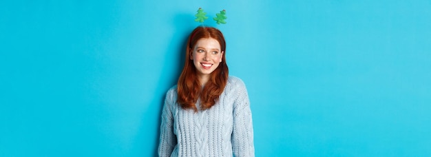 Bezpłatne zdjęcie zimowe wakacje i koncepcja sprzedaży świątecznej śliczna ruda dziewczyna w śmiesznym nowym roku z pałąkiem na głowę uśmiechnięta toaleta