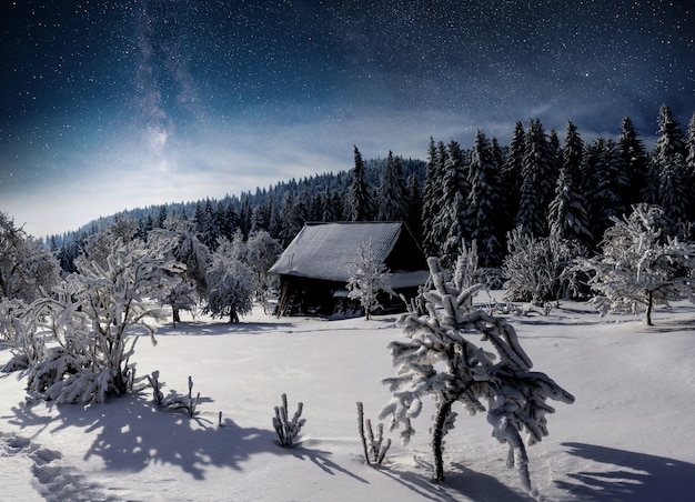 Zimowy krajobraz. Górska wioska w ukraińskich Karpatach. Wibrujące nocne niebo z gwiazdami, mgławicą i galaktyką. Astrofotografia głębokiego nieba