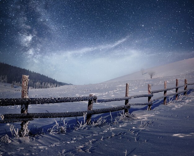 Zimowy krajobraz. Górska wioska w ukraińskich Karpatach. Wibrujące nocne niebo z gwiazdami, mgławicą i galaktyką. Astrofotografia z głębokiego nieba