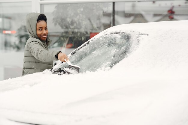 Zimowy portret afrykańskiej kobiety sprzątanie śniegu z samochodu. Kobieta w zielonej kurtce.