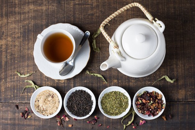 Ziołowa filiżanka herbaty i czajnik z miseczkami herbacianych ziół na drewnianym biurku