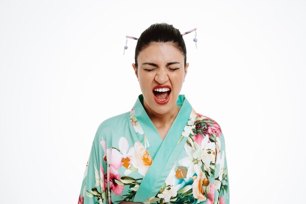zła młoda gejsza kobieta w tradycyjnym japońskim kimonie krzycząca z rozdrażnionym wyrazem szaleństwa stojąc nad białą ścianą