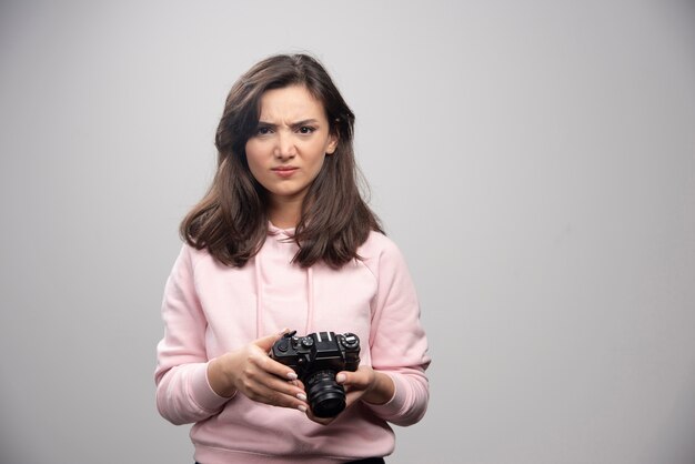 Zły fotograf trzymając aparat na szarej ścianie.