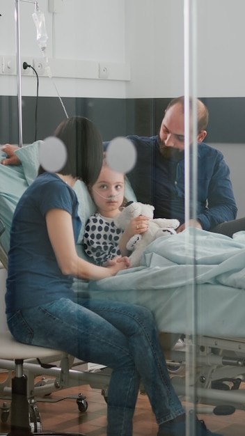 Bezpłatne zdjęcie zmartwieni rodzice siedzą z chorą córką czekając na ekspertyzę dotyczącą choroby podczas badania lekarskiego...