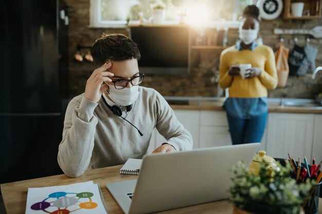 Zmartwiony biznesmen z maską na twarz czyta problematyczne e-maile na laptopie w domu