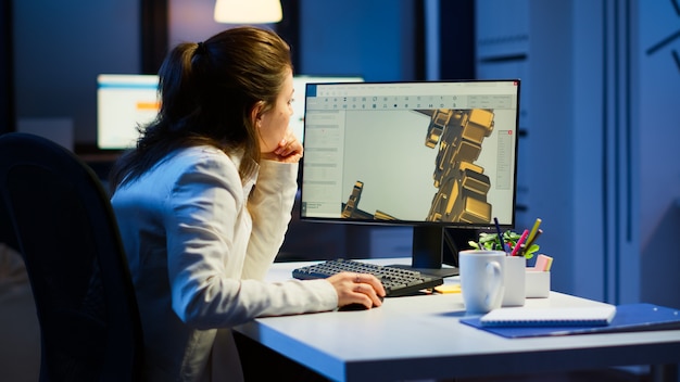 Zmęczona kobieta architekt pracujący nad nowoczesnym programem cad w godzinach nadliczbowych siedząc przy biurku w biurze start-up. Inżynier przemysłowy studiujący pomysł prototypu na komputerze pokazujący oprogramowanie cad na wyświetlaczu urządzenia