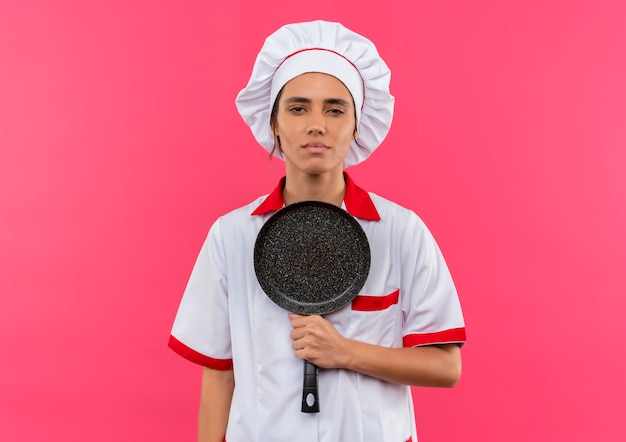 Bezpłatne zdjęcie zmęczona młoda kobieta kucharz ubrana w mundur szefa kuchni trzymając patelnię z miejsca na kopię