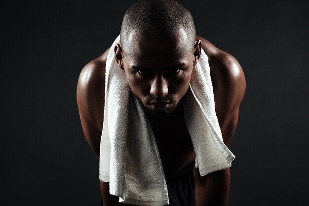 Zmęczony afro amerykański sportowiec z ręcznikiem na ramionach, relaks po treningu