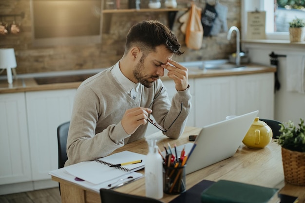 Zmęczony freelancer odczuwa ból głowy po pracy przy komputerze w domu