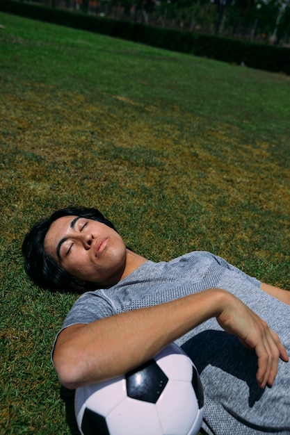 Bezpłatne zdjęcie zmęczony mężczyzna leży z oczami zamkniętymi na trawie z piłką nożną