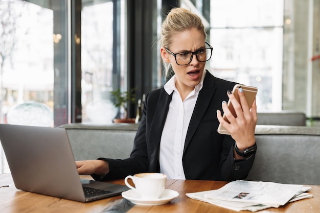 Zmieszana biznesowa kobieta używa laptop i telefon