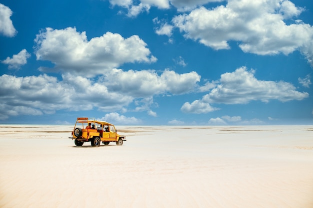 Żółta ciężarówka jedzie po piaszczystej ziemi pod zachmurzonym błękitnym niebem