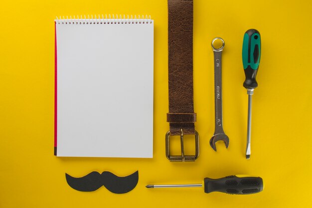 Żółta powierzchnia z pustym notatnikiem i narzędziami na dzień ojca