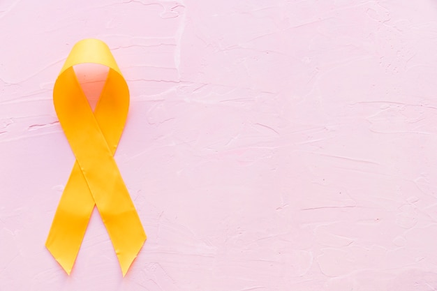 Żółta wstążka symboliczny kolor raka kości sarkomeru na różowym tle