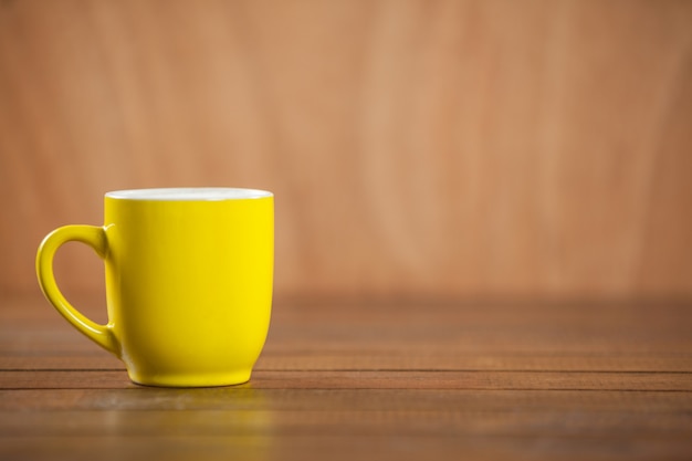 Żółty kubek kawy na drewnianym stole