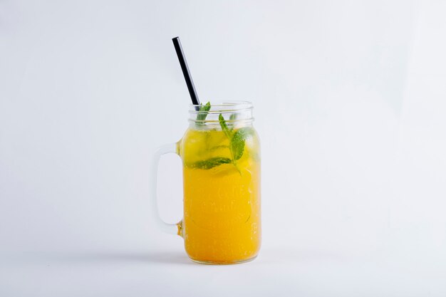 Żółty sok pomarańczowy w szklanym słoju z liśćmi mięty.