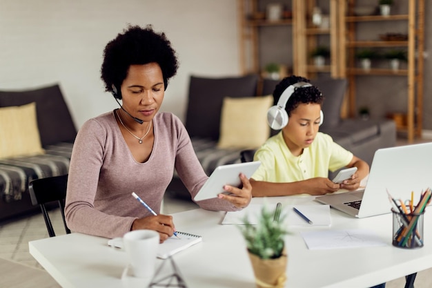 Zostań w domu mama pracująca na touchpadzie, podczas gdy jej syn korzysta ze smartfona