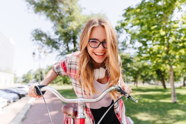 Zrelaksowana długowłosa dziewczyna w słuchawkach, jazda na rowerze. Wspaniała pani z uroczym uśmiechem siedzi na rowerze.