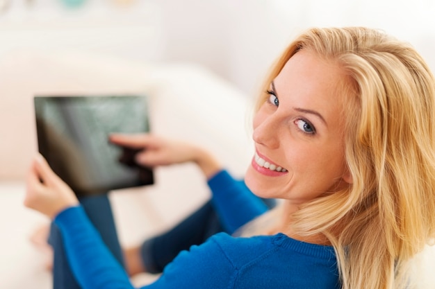 Zrelaksowana kobieta siedzi na kanapie z cyfrowym tabletem