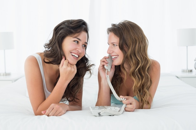 Zrelaksowani młodzi żeńscy przyjaciele używa telefon w łóżku