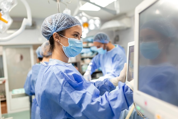 Zróżnicowany zespół profesjonalnych chirurgów wykonujących chirurgię inwazyjną pacjenta w szpitalnej sali operacyjnej Pielęgniarka podaje narzędzia chirurgowi Anestezjolog monitoruje stany życiowe