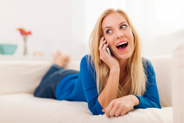 Zszokowana kobieta, leżąc na kanapie i rozmawiając przez telefon
