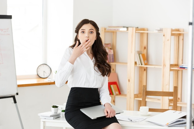 Zszokowana młoda kobieta biznesu zaskoczona czymś z przodu, siedząc w nowoczesnym biurze