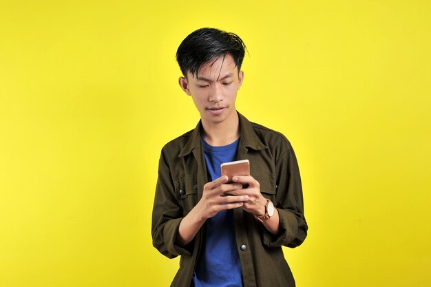 Zszokowana twarz azjatyckiego człowieka w białej koszuli patrząc na ekran telefonu, na białym tle na żółtym tle.
