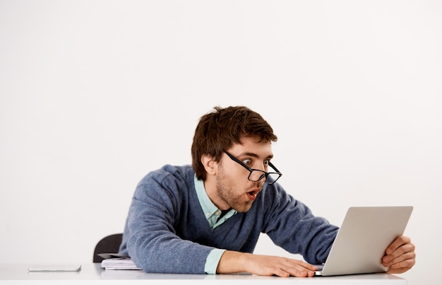 Zszokowany, zaskoczony i pod wrażeniem pracownik biurowy, mężczyzna przedsiębiorca siedzący przy biurku, wpatrujący się w ekran laptopa bez słowa, czytający dobre wieści