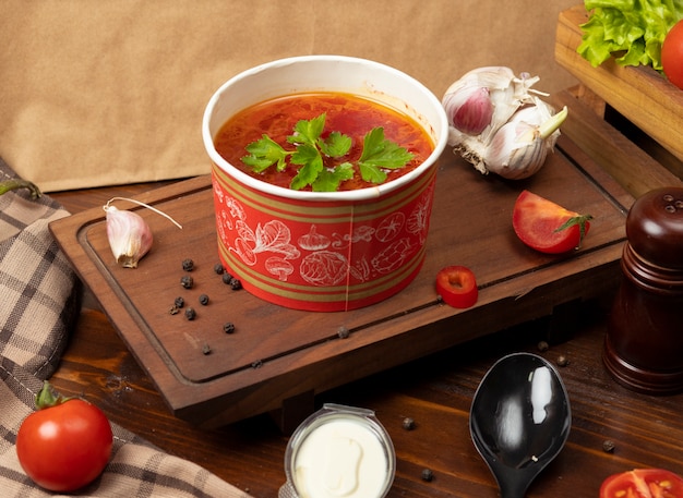 Zupa pomidorowa, barszczowa w misce jednorazowego użytku z zielonymi warzywami.